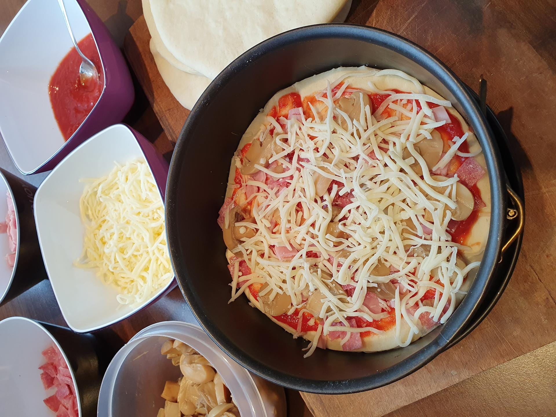 Geben Sie darauf zuerst die Tomatensoße, dann Salami und Schinken sowie die Pilze. Am Ende bestreuen Sie das Ganze mit etwas Käse.