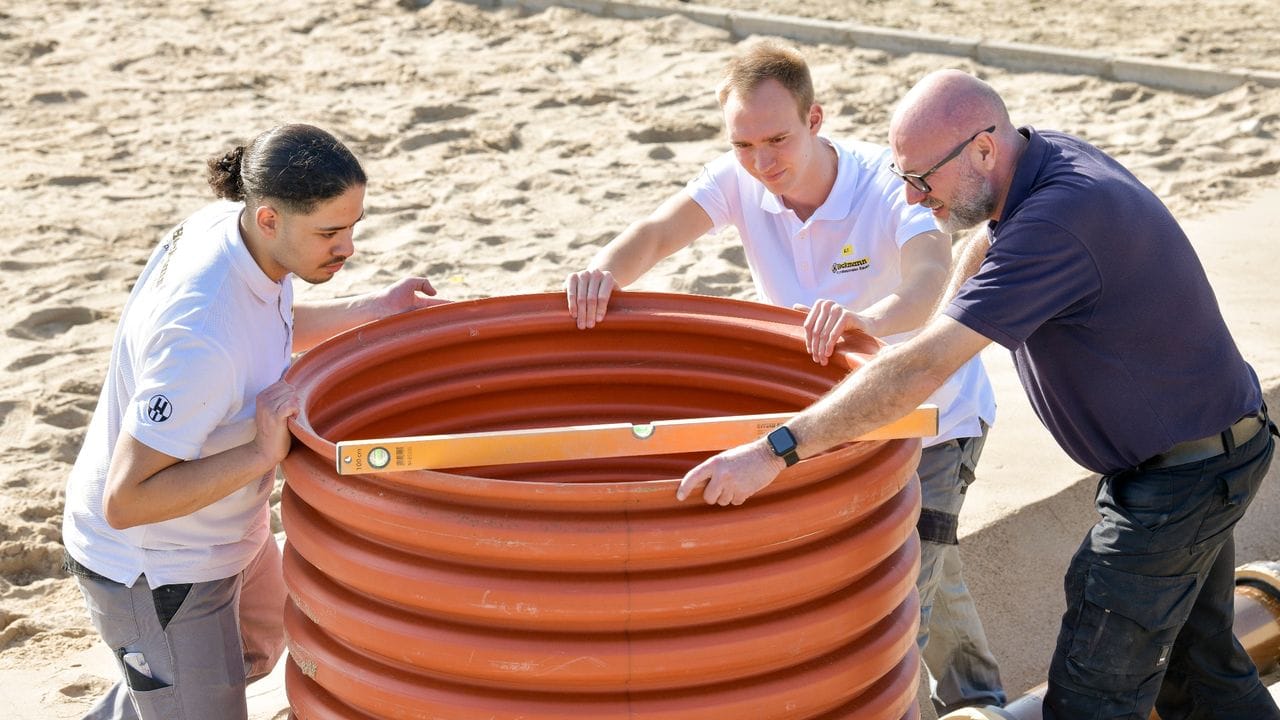 Die angehenden Kanalbauer Issam Bhihi und Steffen Hallermann prüfen gemeinsam mit Ausbilder Gunther Sibilski ein grosses Polyethylenrohr.