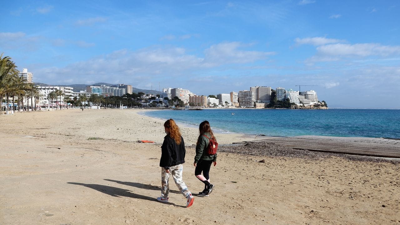 Zwei junge Frauen gehen am leeren Strand von Magaluf entlang.