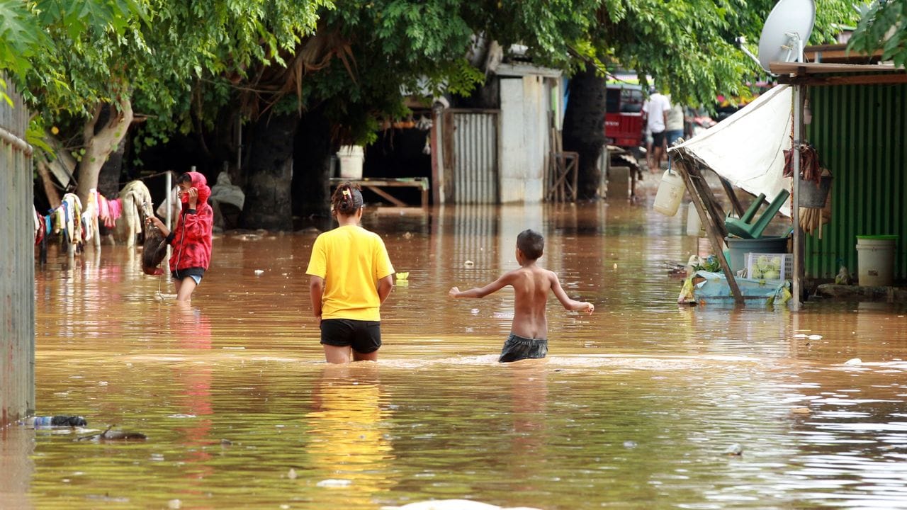 Menschen waten in Dili durch das Hochwasser.