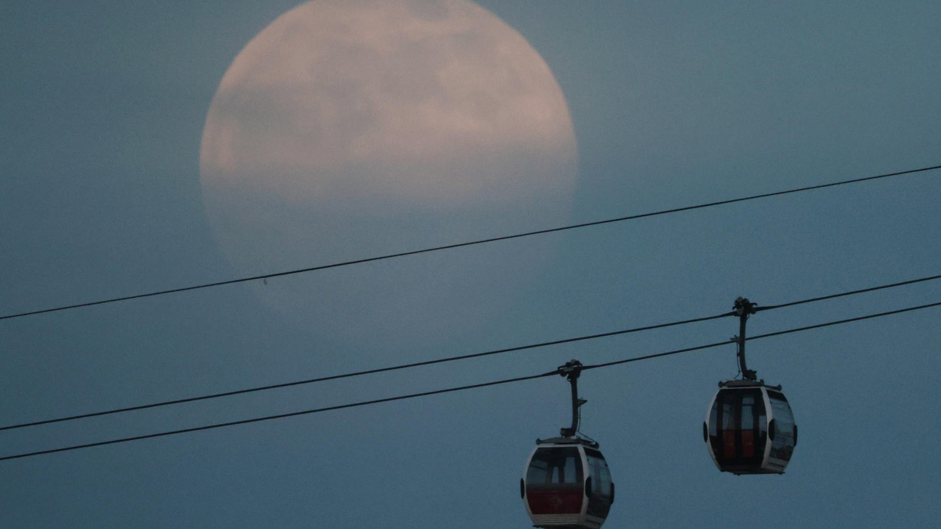 England, London: Der Vollmond zeigt sich hinter einer Seilbahn.