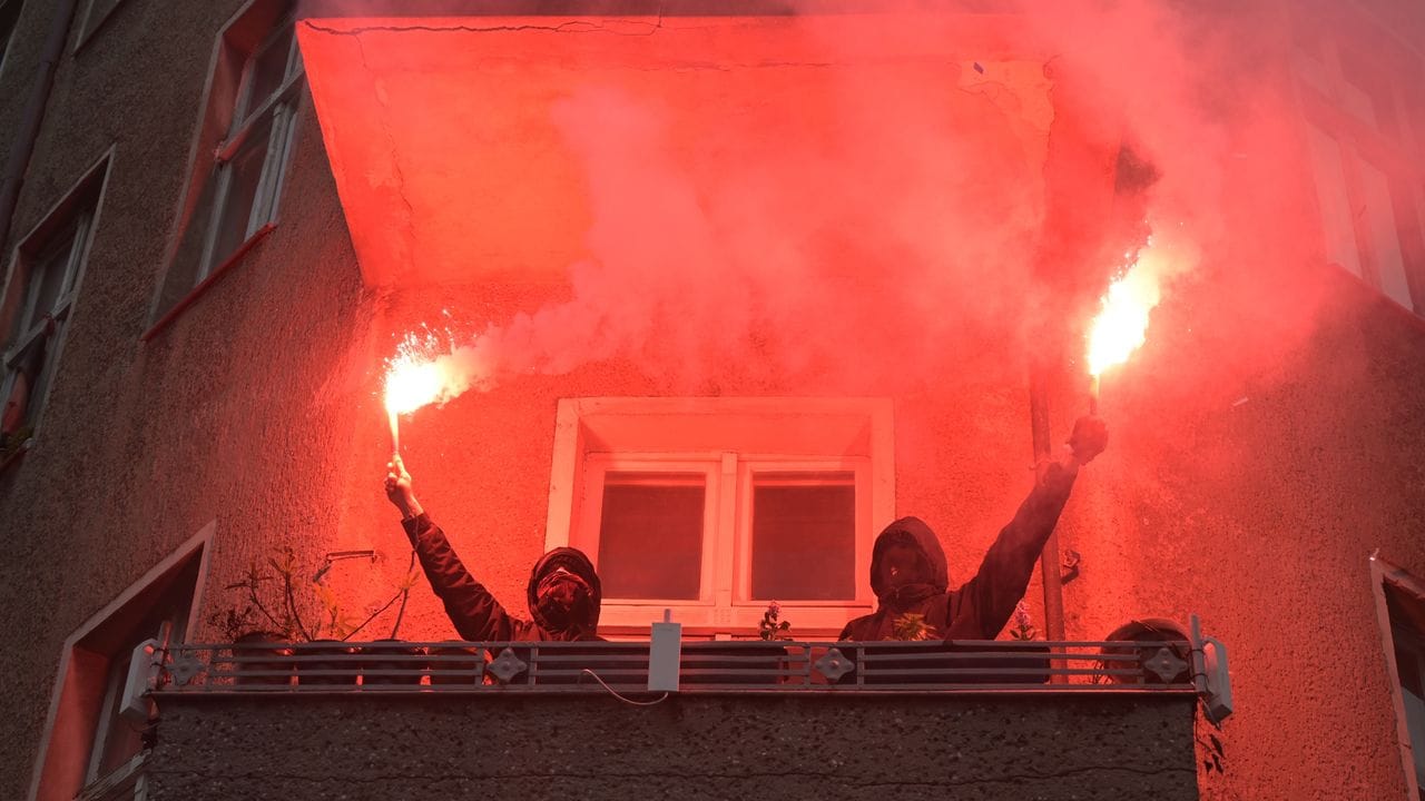 Zwei Personen halten während einer Demonstration linker und linksradikaler Gruppen durch Wedding zwei brennende Rauchfackeln auf einem Balkon.