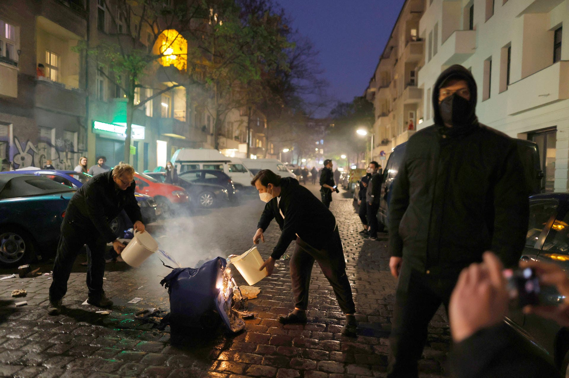 Anwohner löschen eine brennende Barrikade in Neukölln: Die Polizei will am Sonntag Bilanz ziehen.