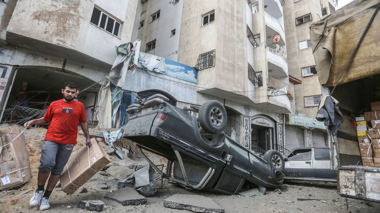 Ein Mann geht an einem umgestürtzen Autowrack vor einem Wohnhaus, welches zuvor von israelischen Luftangriffen getroffen wurde, vorbei.