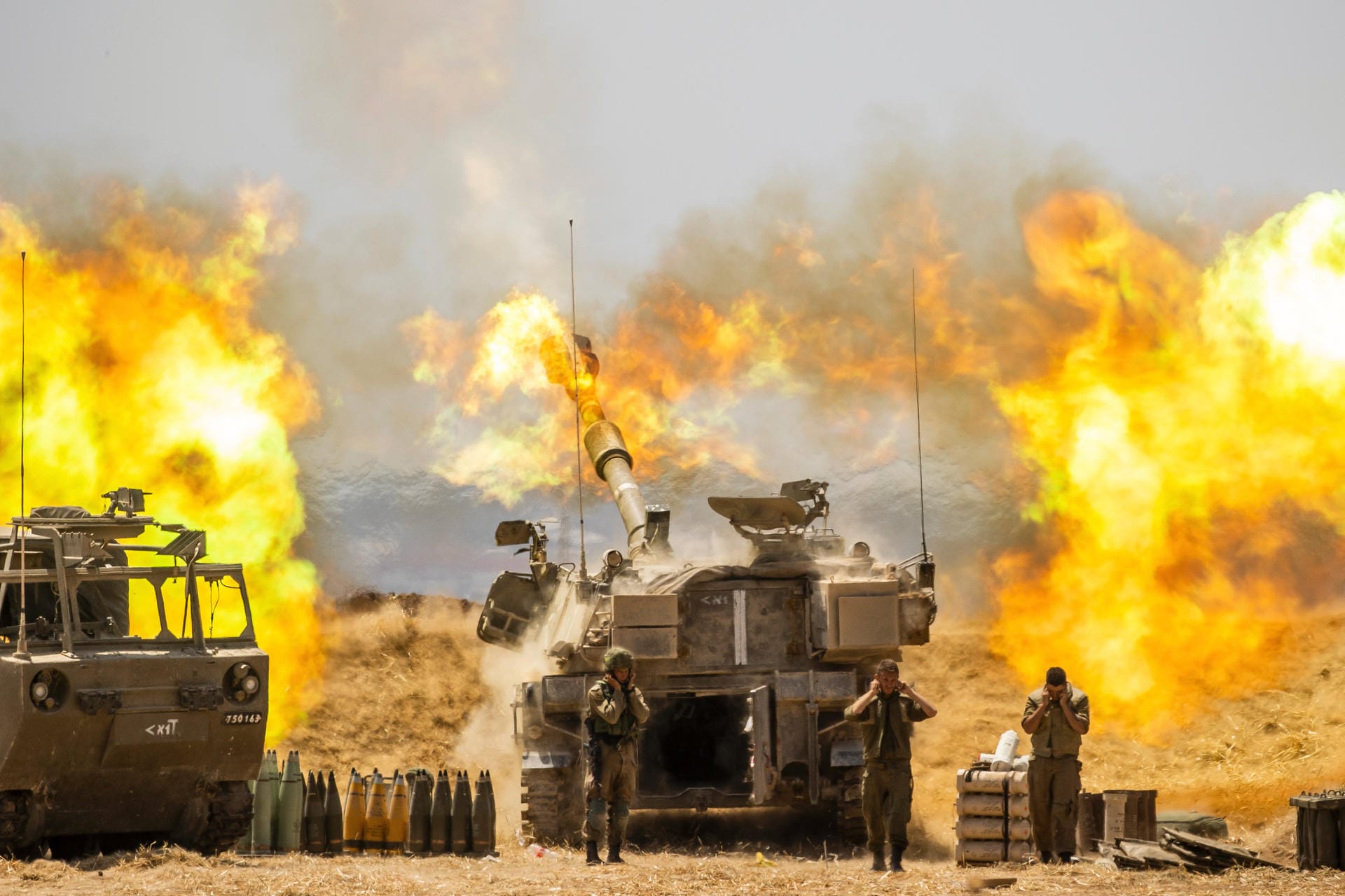 Israel: Drei israelische Soldaten halten sich die Ohren zu, während ein Artilleriegeschütz auf Ziele im Gazastreifen feuert.