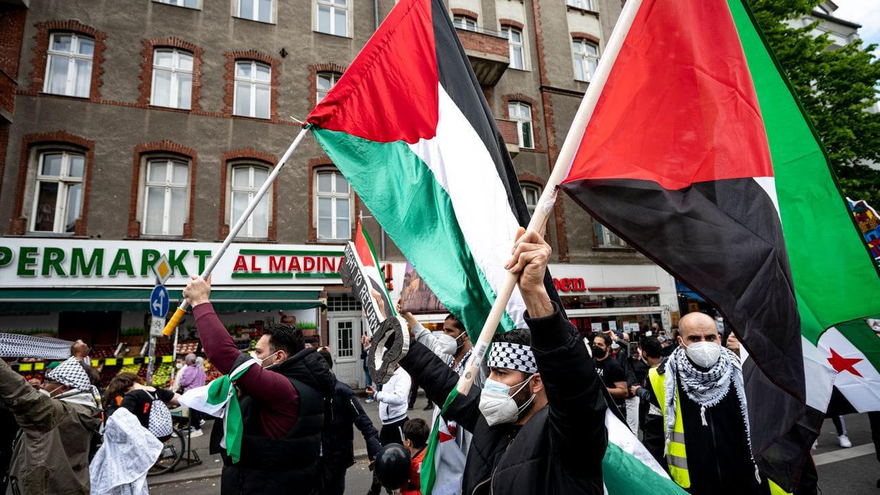 Teilnehmer einer Demonstration verschiedener palästinensischer Gruppen laufen mit Palästina-Flaggen durch Neukölln.