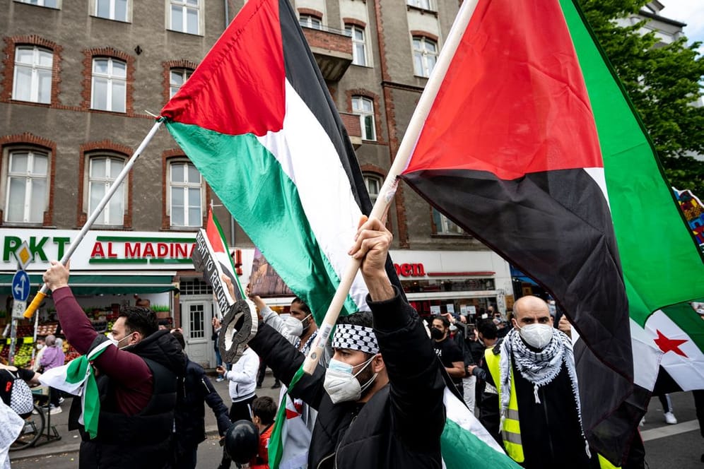 Teilnehmer einer Demonstration verschiedener palästinensischer Gruppen laufen mit Palästina-Flaggen durch Neukölln.