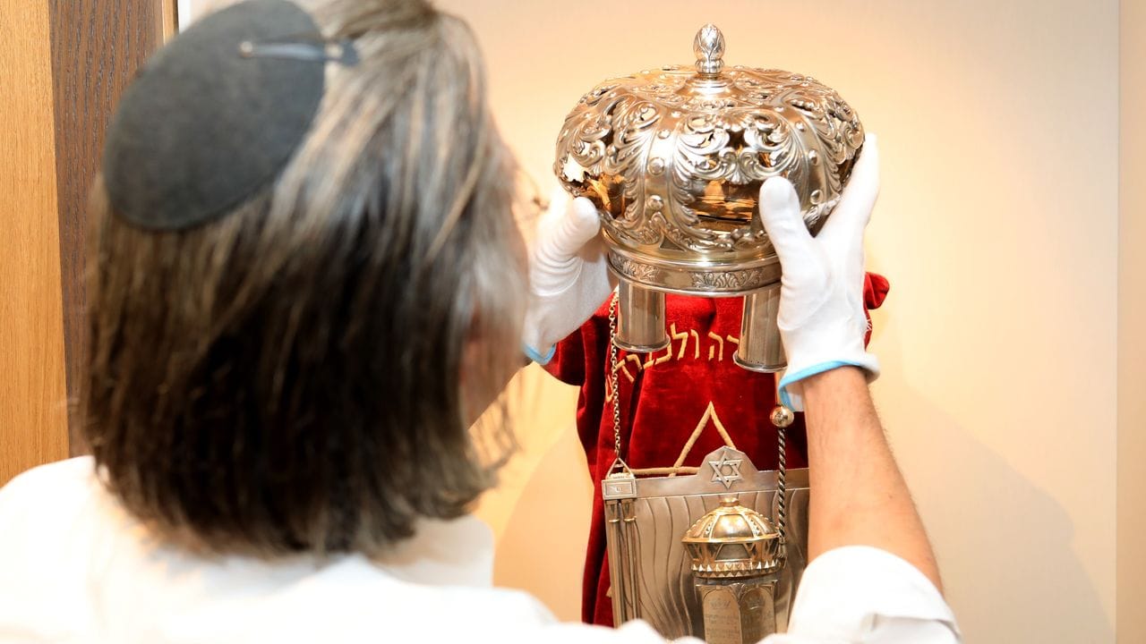 Der Kurator Uri Faber setzt eine Krone auf eine Torarolle mit Mantel im Berend Lehmann Museum in Halberstadt.
