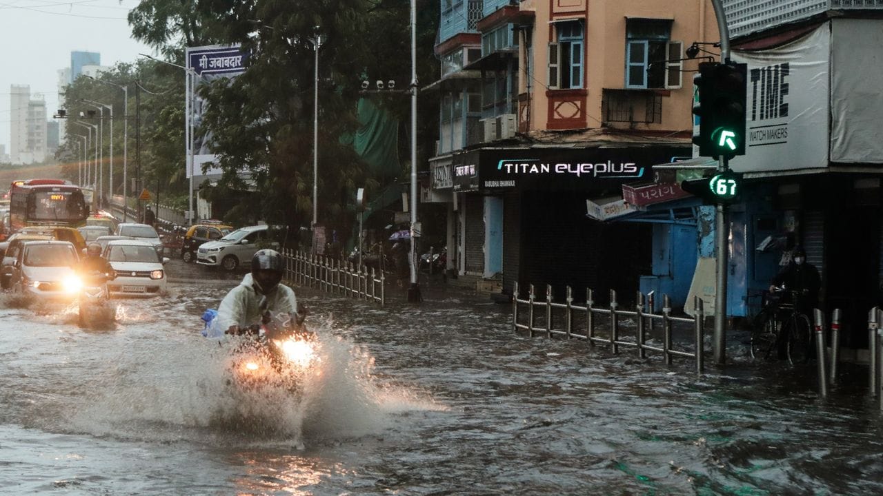 Pendler fahren in Mumbai auf einer überschwemmten Straße.