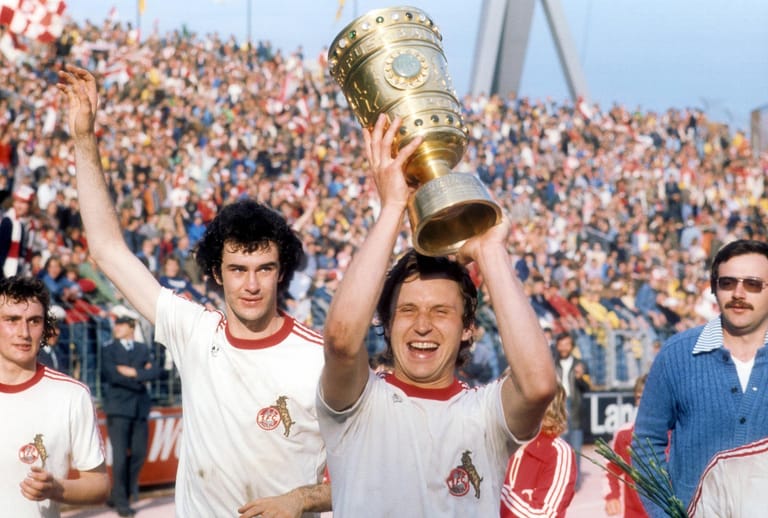 Im Jahre 1977 hieß der Pokalsieger dann erneut 1. FC Köln. Das erste Finale endete 1:1 und hatte auch nach der Verlängerung keinen Sieger. Da es Elfmeterschießen damals noch nicht gab, kam es zum Wiederholungsspiel. Dies gewannen die Kölner in Hannover mit 1:0 gegen Hertha BSC. Heinz Flohe reckt den Pokal in die Höhe, sein Teamkollege Gerd Strack freut sich mit.