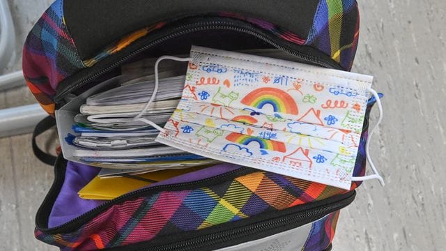 Eine Maske liegt auf dem Rucksack eines Grundschülers. Eine Maske liegt auf dem Rucksack eines Grundschülers.