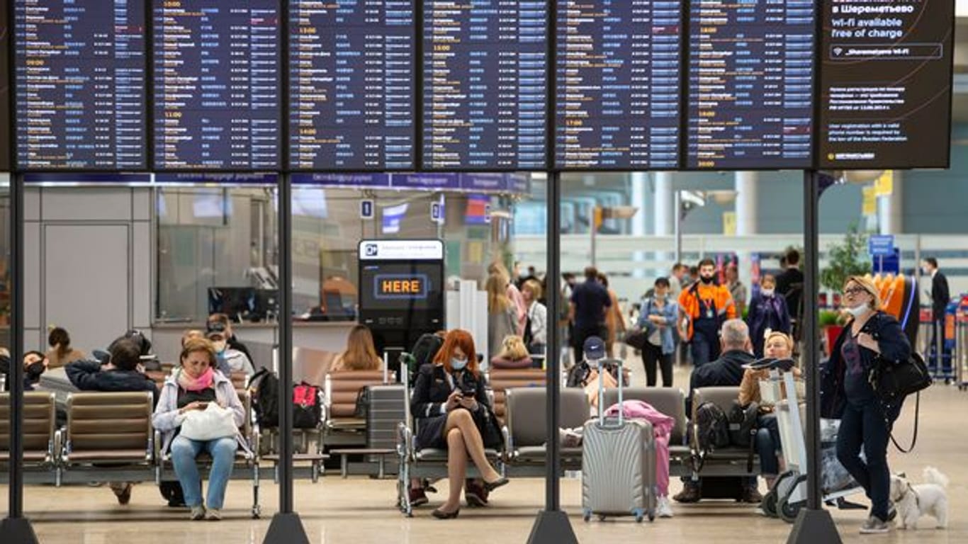 Passagiere sitzen auf dem internationalen Flughafen Scheremetjewo in Moskau unter einer Fluginformationstafel.