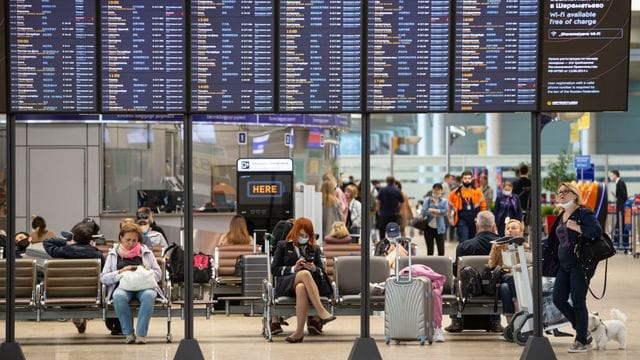 Passagiere sitzen auf dem internationalen Flughafen Scheremetjewo in Moskau unter einer Fluginformationstafel. Passagiere sitzen auf dem internationalen Flughafen Scheremetjewo in Moskau unter einer Fluginformationstafel.