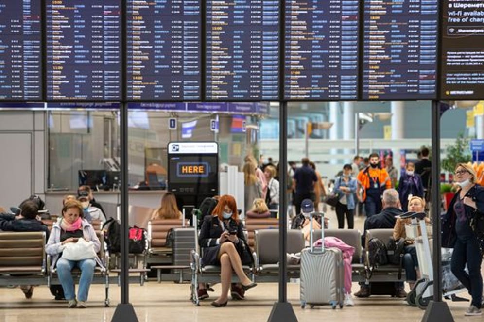 Passagiere sitzen auf dem internationalen Flughafen Scheremetjewo in Moskau unter einer Fluginformationstafel.