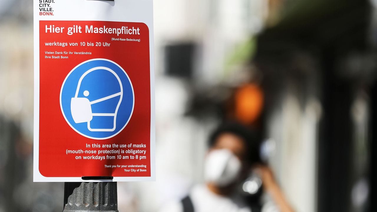 Ein Schild mit der Aufschrift "Hier gilt Maskenpflicht" hängt in der Fußgängerzone in Bonn. Ein Schild mit der Aufschrift "Hier gilt Maskenpflicht" hängt in der Fußgängerzone in Bonn.