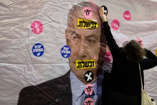 Ein Plakat mit dem Konterfei von Israels Premierminister Netanjahu wird mit Aufklebern überklebt.
