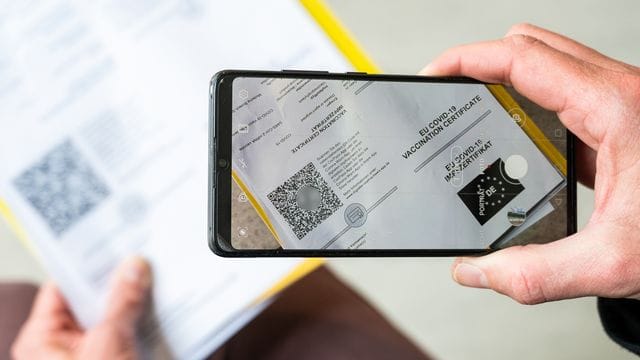 Ein Mann scannt mit einem Handy ein Dokument für den Digitalen Impfnachweis. Ein Mann scannt mit einem Handy ein Dokument für den Digitalen Impfnachweis.