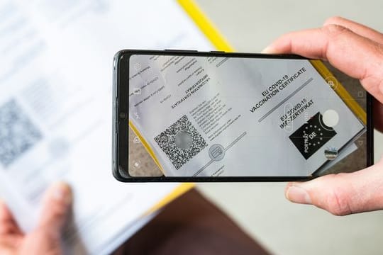 Ein Mann scannt mit einem Handy ein Dokument für den Digitalen Impfnachweis.