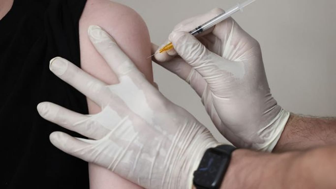 Ein Arzt impft in seiner Praxis einen Jugendlichen mit dem Serum von Biontech/Pfizer.