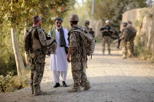 Ein Bundeswehrsoldat (l) und ein Dolmetscher (r) sprechen nahe Kundus im Distrikt von Char Darreh mit einem Mann.