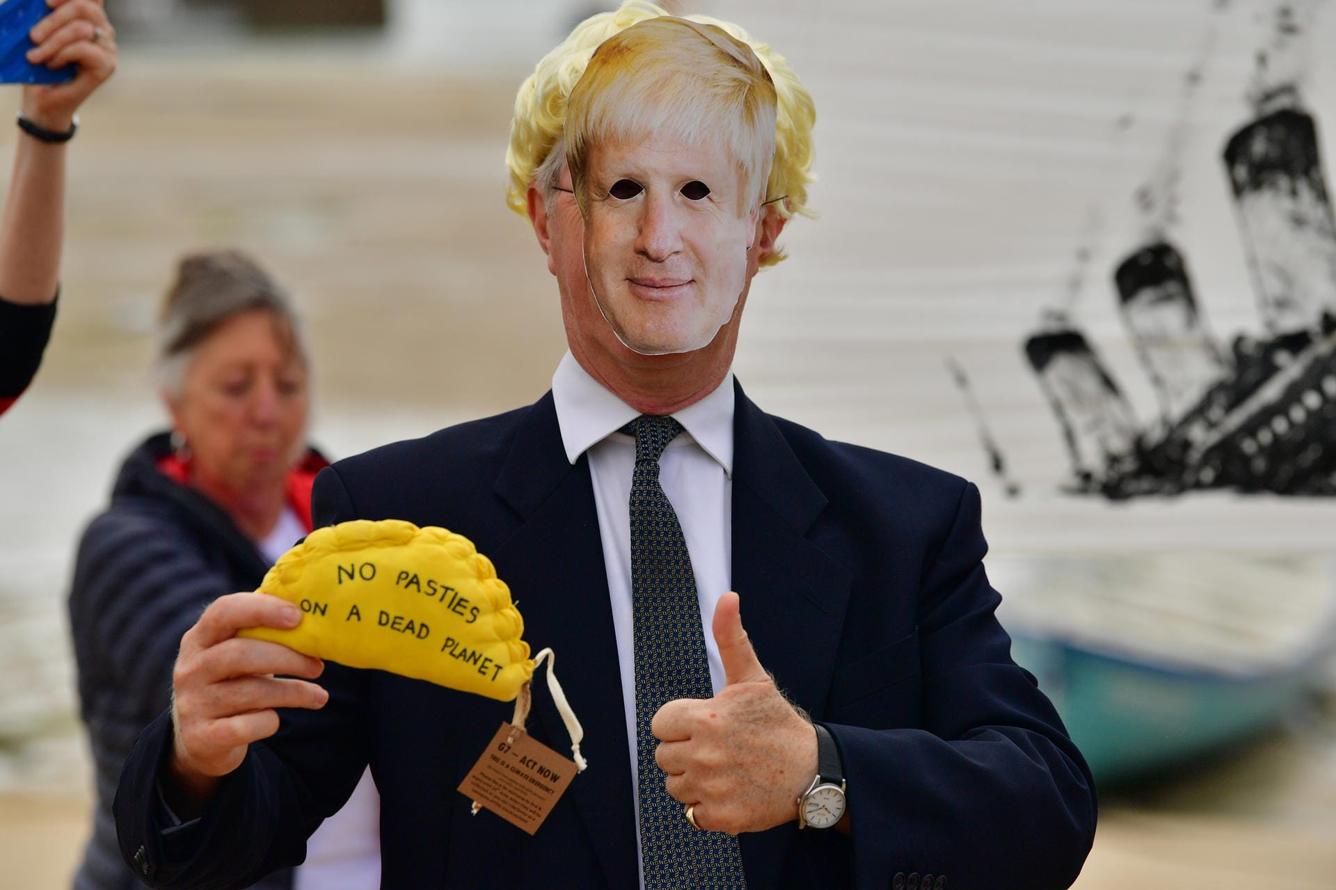 Ein Aktivist von Extinction Rebellion trägt eine Pappmaske mit dem Conterfeit von Großbritanniens Premierminister Boris Johnson. In der Hand hält er eine "Protest-Pastete". Gefüllte Teigtaschen sind in Cornwall eine regionale Spezialität, die genähte Variante trägt den Spruch: "Keine Pasteten auf einem toten Planeten".