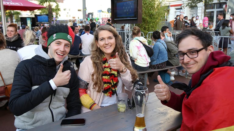 Guter Dinge vor dem Spiel: Jakub (l-r), Lisa und Alex sitzen bei einem Public Viewing auf dem Spielbudenplatz an der Hamburger Reeperbahn an einem Tisch zusammen.