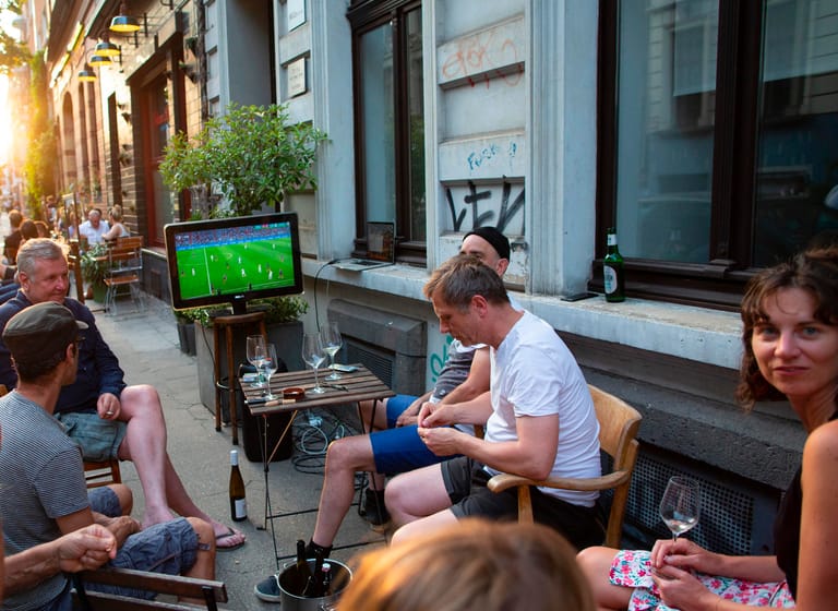 Menschen sitzen auf der Elsaßstraße: Auch in kleinerem Kreis lässt sich gemeinsam Fußball schauen.