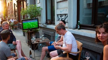 Menschen sitzen auf der Elsaßstraße: Auch in kleinerem Kreis lässt sich gemeinsam Fußball schauen.
