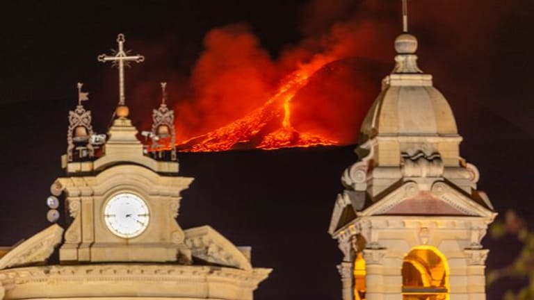 Hinter der Kirche Santa Maria della Guardia in Belpasso bei Catania bricht Lava aus einem Krater des Ätna.