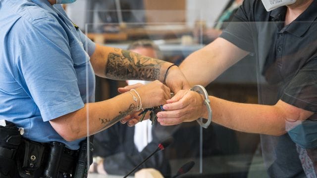 Eine Justizbeamtin (l) nimmt dem Angeklagten die Handschellen ab. Eine Justizbeamtin (l) nimmt dem Angeklagten die Handschellen ab.