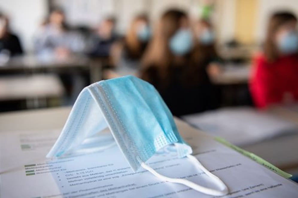 Eine Maske liegt im Unterricht an einem Gymnasium in München auf Schulunterlagen.