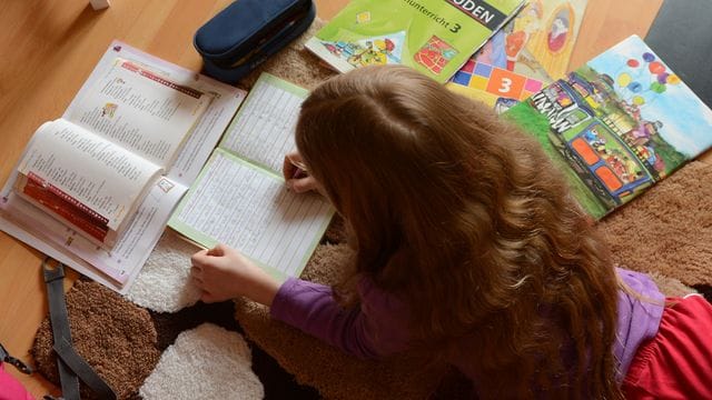 Ein Mädchen liegt auf einem Teppich in seinem Kinderzimmer und erledigt seine Hausaufgaben im Fach Deutsch. Ein Mädchen liegt auf einem Teppich in seinem Kinderzimmer und erledigt seine Hausaufgaben im Fach Deutsch.