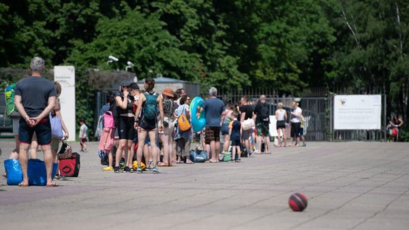 Menschen stehen bei warmem Wetter in einer Schlange vor dem Eingang zum Olympiabad in Berlin.