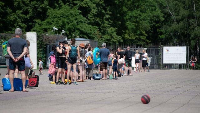 Menschen stehen bei warmem Wetter in einer Schlange vor dem Eingang zum Olympiabad in Berlin. Menschen stehen bei warmem Wetter in einer Schlange vor dem Eingang zum Olympiabad in Berlin.