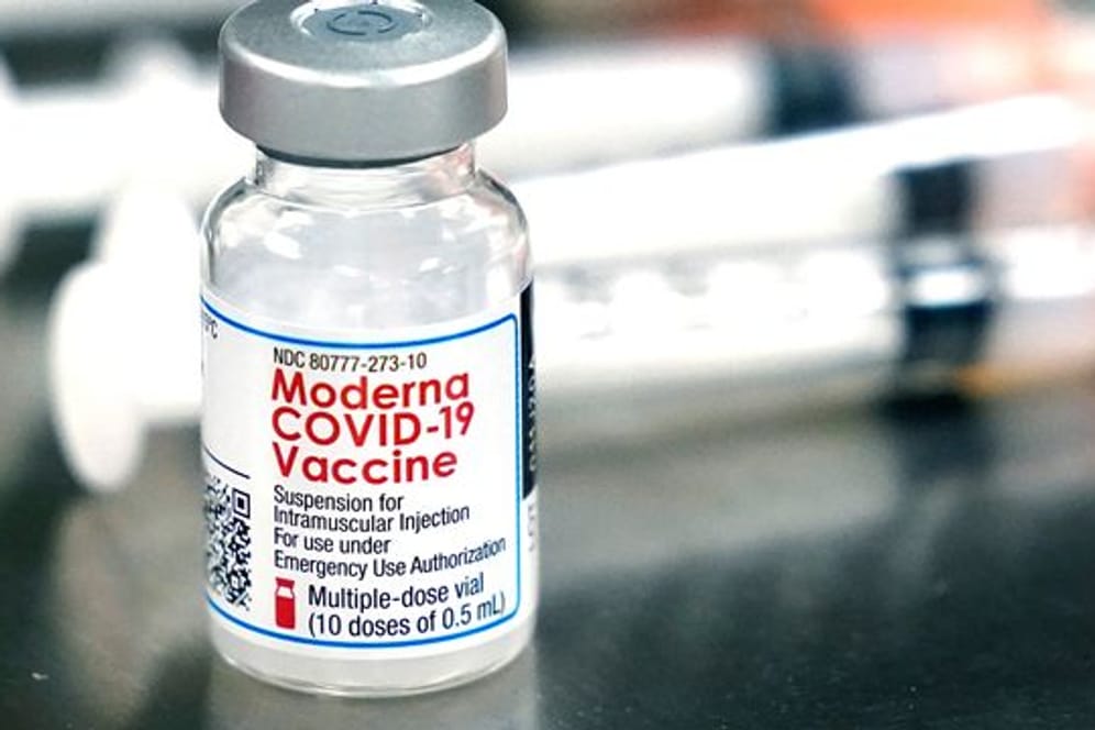 Ein Fläschchen des Moderna-Impfstoffes steht neben Spritzen.