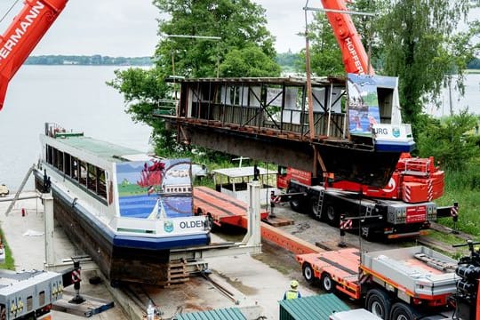 Zwei Mobilkrane heben ein Teilstück des längsseitig zersägten Fahrgastschiffes "MS Oldenburg" am Zwischenahner Meer auf einen Tieflader.