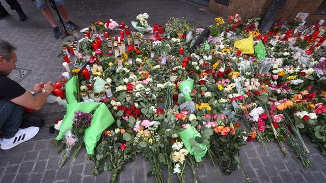 Ein Mann entzündet vor einem geschlossenen und abgesperrten Kaufhaus in der Innenstadt eine Kerze.
