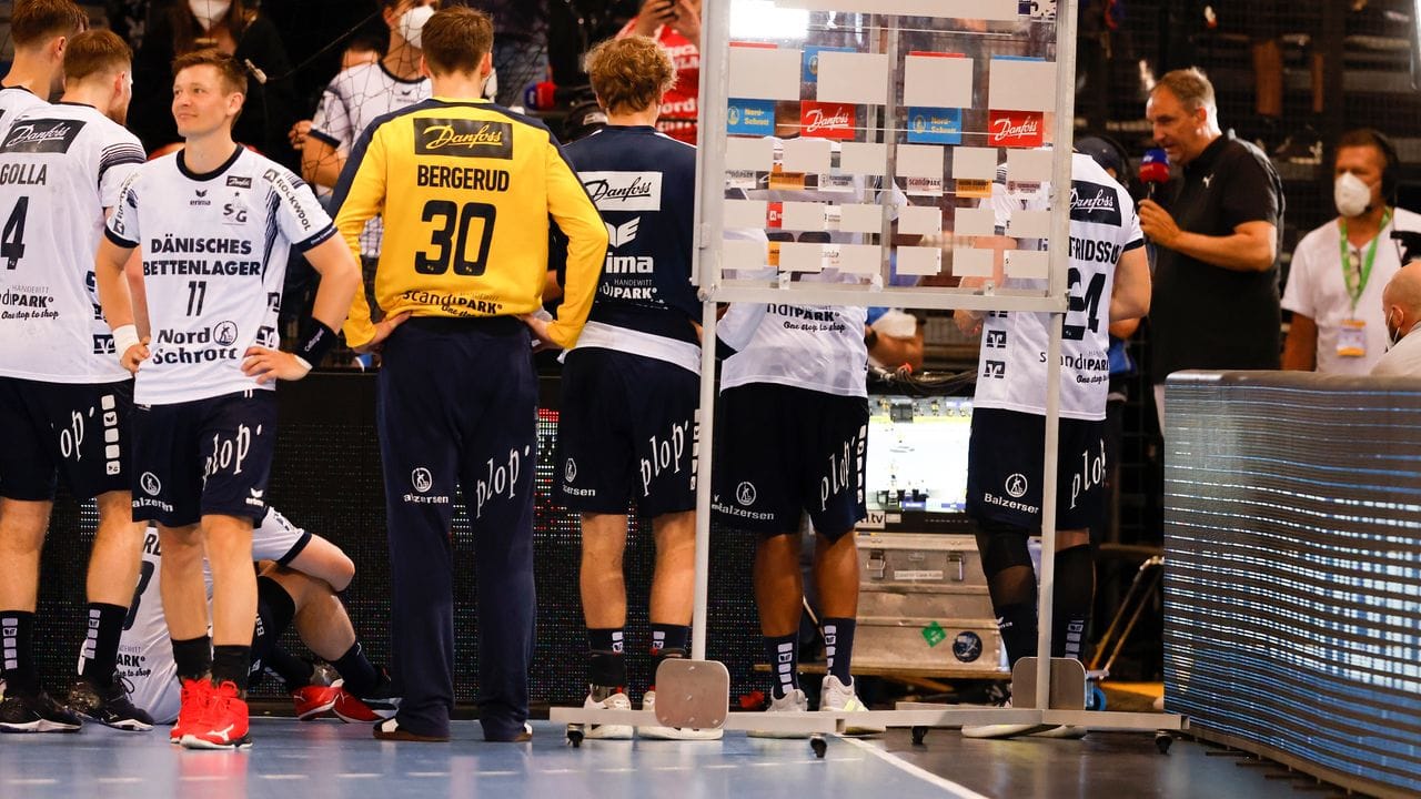 Die Flensburger Spieler stehen nach ihrem Sieg vor einem Fernseher und schauen das Spiel der Kieler in Mannheim.