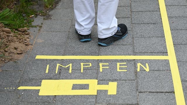 Ein Mann steht hinter einer Bodenmarkierung "Impfen"