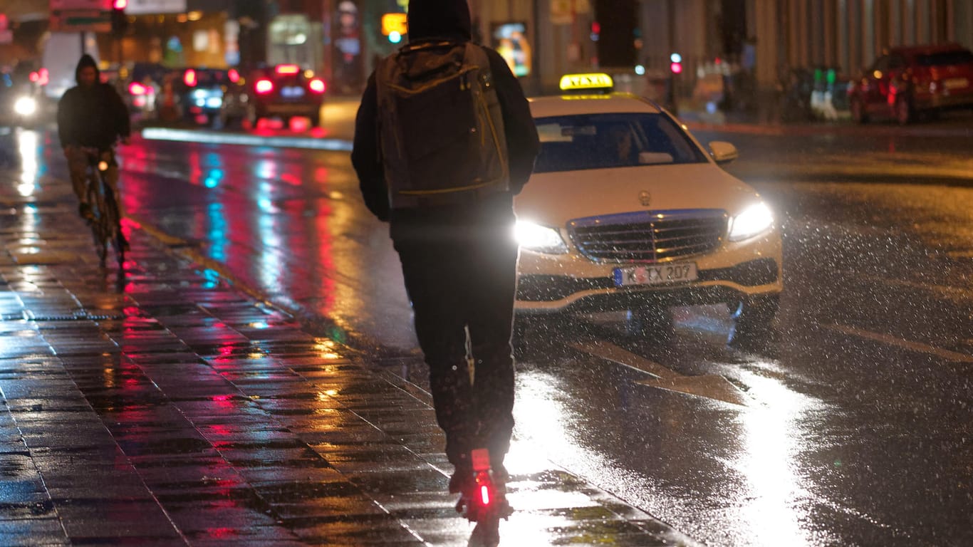 Ein Fahrer fährt auf einem E-Scooter bei Regenwetter durch die Kölner Innenstadt: Die städtische Politik diskutiert über mehr Regeln für die Gefährte.