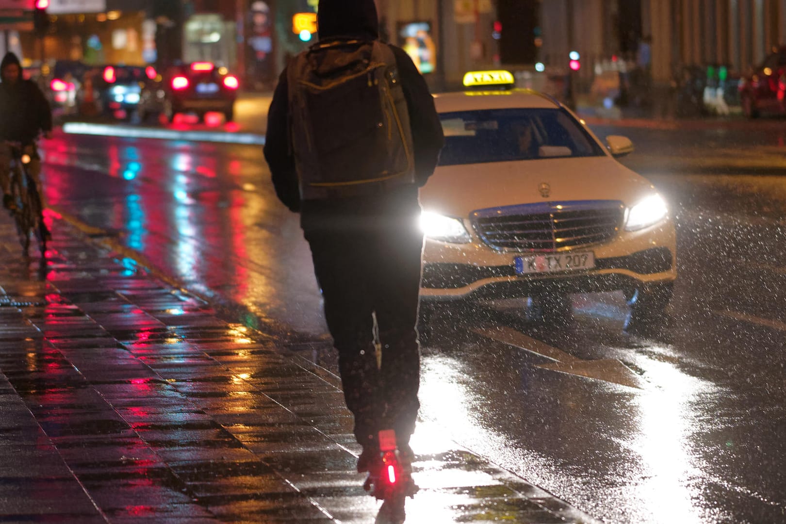 Ein Fahrer fährt auf einem E-Scooter bei Regenwetter durch die Kölner Innenstadt: Die städtische Politik diskutiert über mehr Regeln für die Gefährte.