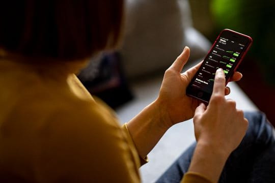 Eine junge Frau beobachtet mit ihrem iPhone die Aktienkurse.