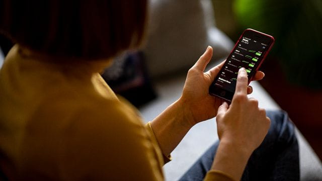 Eine junge Frau beobachtet mit ihrem iPhone die Aktienkurse.