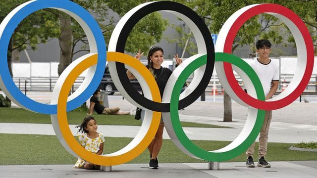 Menschen stehen stehen hinter den Olympischen Ringen in Tokio