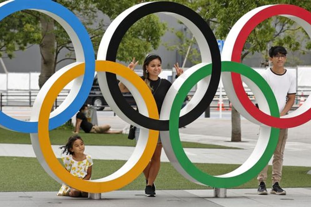 Menschen stehen stehen hinter den Olympischen Ringen in Tokio