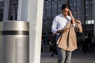 Frau schaut erschrocken auf ihr Smartphone: WLAN-Name gefährdet iPhones