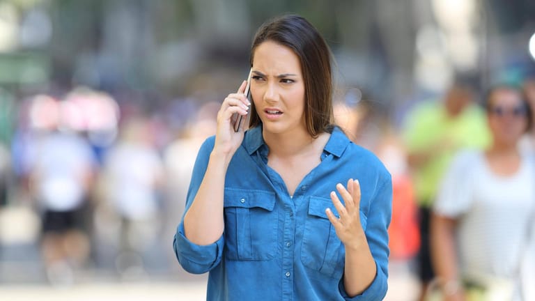 Eine genervte Frau am Handy: Vorsicht vor Spam-Anrufen.