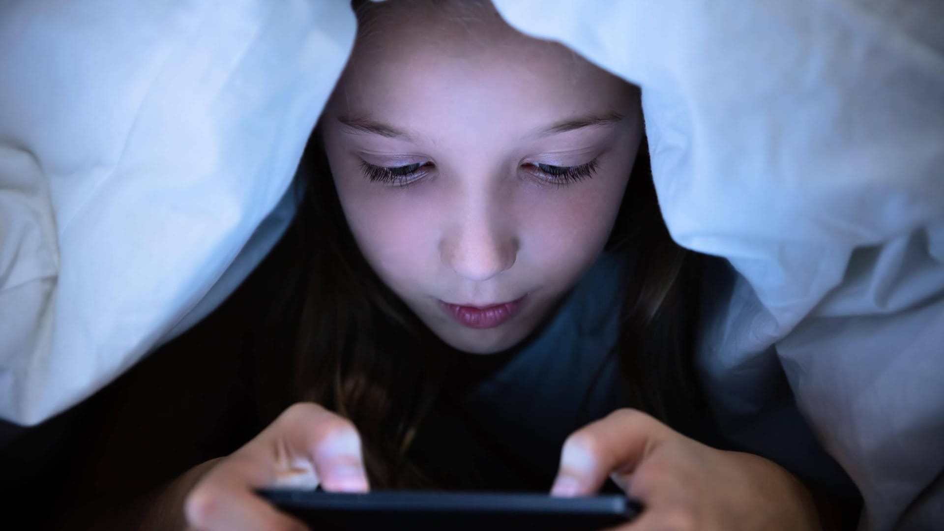 Ein Kind am Smartphone (Symbolbild): Die Firma Tencent will Minderjährige Aus Spielen rauswerfen, wenn sie zu spät noch eingeloggt sind.