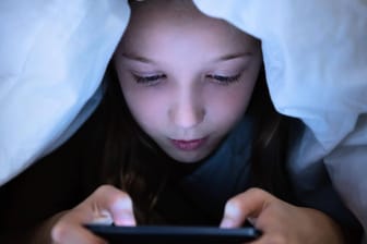 Ein Kind am Smartphone (Symbolbild): Die Firma Tencent will Minderjährige Aus Spielen rauswerfen, wenn sie zu spät noch eingeloggt sind.