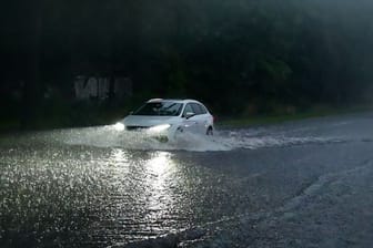 Ein Auto fährt durch eine überflutete Straße